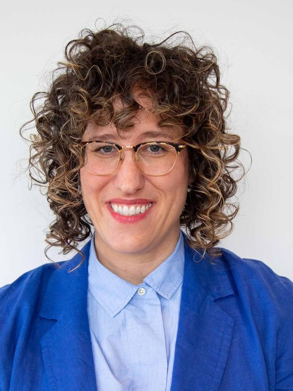 white background, woman wearing glasses, curly hair, blue blazer and light blue collared shirt