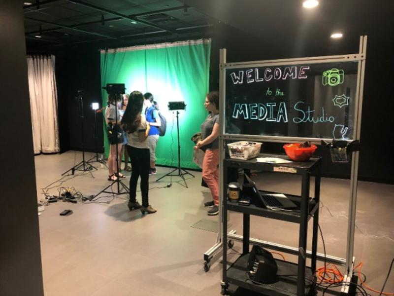 Media studio. Students stand near a green screen and cameras.
