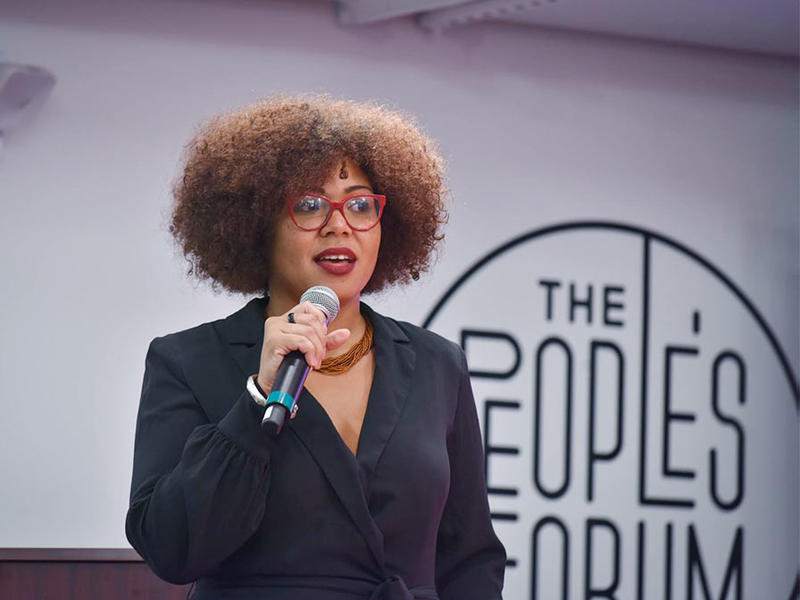 A young Black woman holding a microphone, speaking at an event